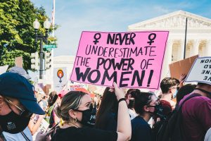 Someone in a crowd at a protest holds a sign above their head. It reads: never underestimate the power of women!