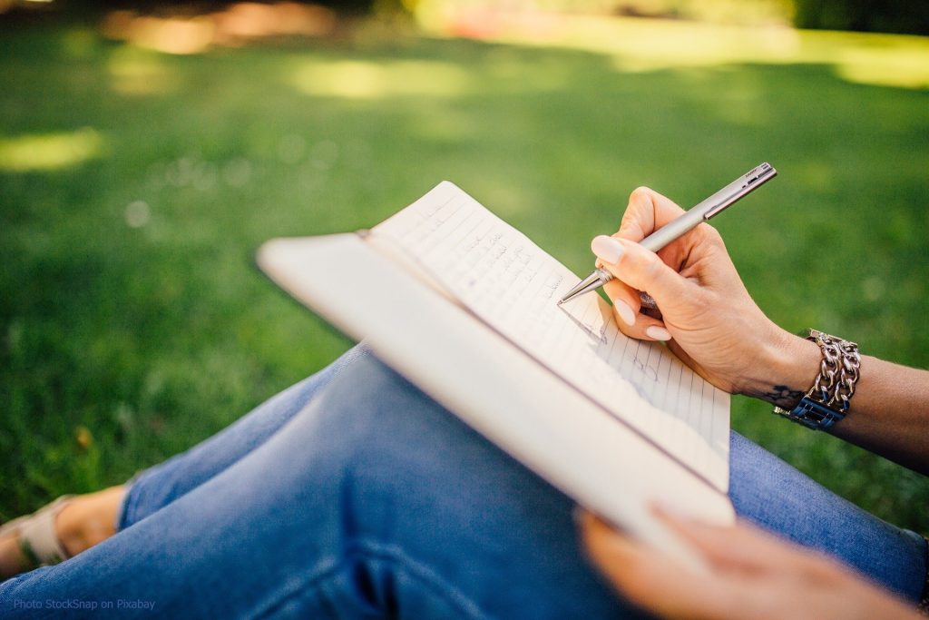 Writing in a notebook while sitting on a lawn