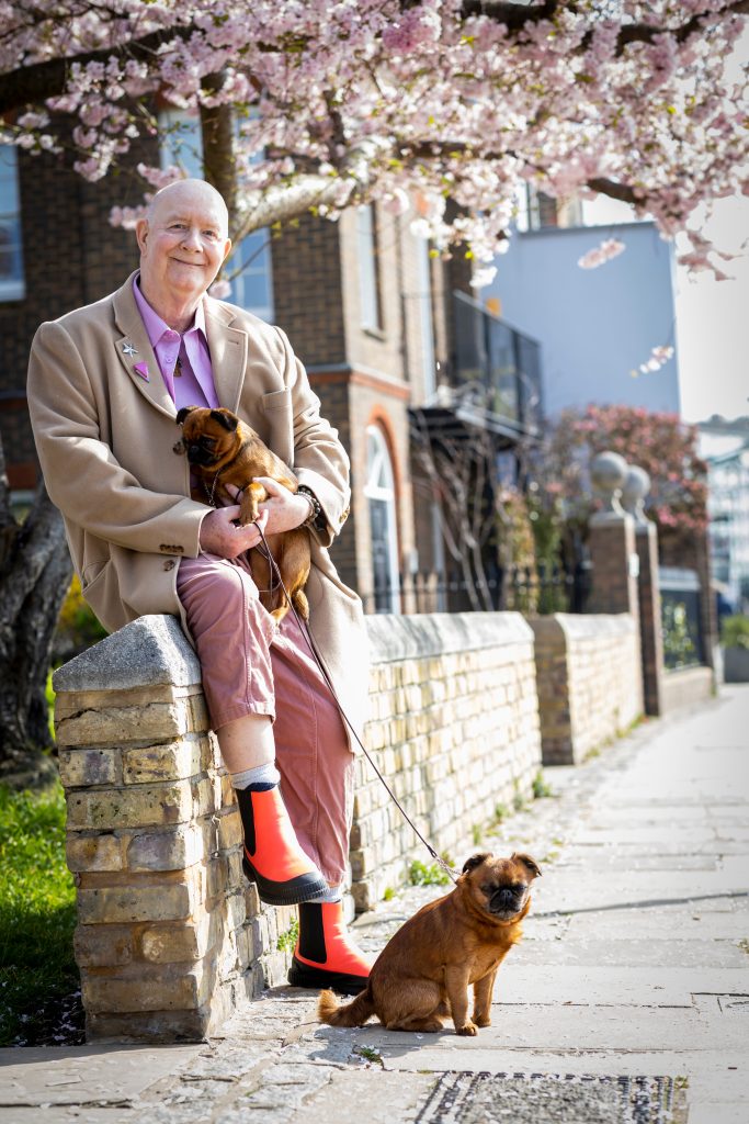 Someone smiles at the camera while sitting outside on a wall with two small dogs. 