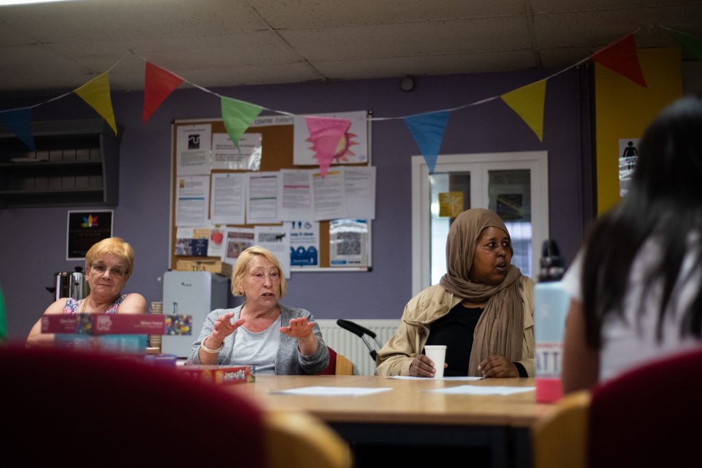 Image shows people sat around a table in a community centre talking.