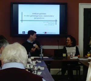 Image of John Appleby and Saskia Hendrinks sitting behind a desk in front of a screen displaying a presentation screen which reads 'Artificial Gametes, In Vitro Gametogenesis: Stakeholders' Perspectives'