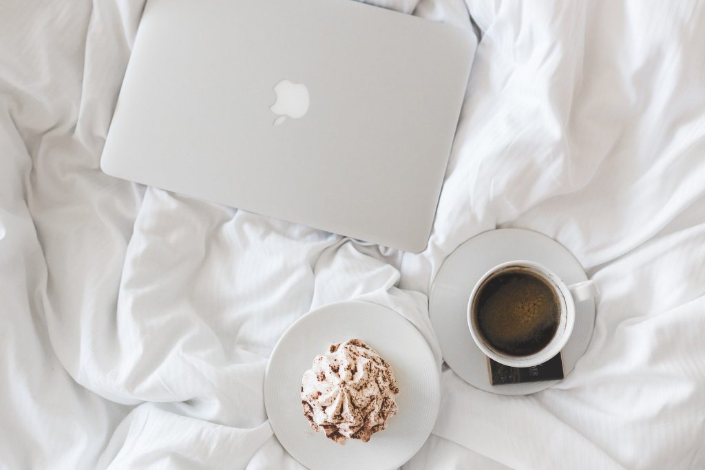 Coffe, muffin and laptop on bed