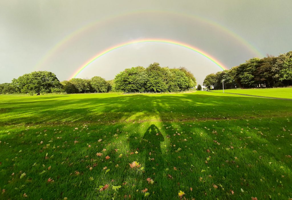 A double rainbow over a green field topped with trees