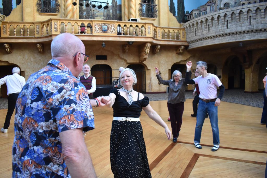 People dancing in pairs in a decorated ball room.