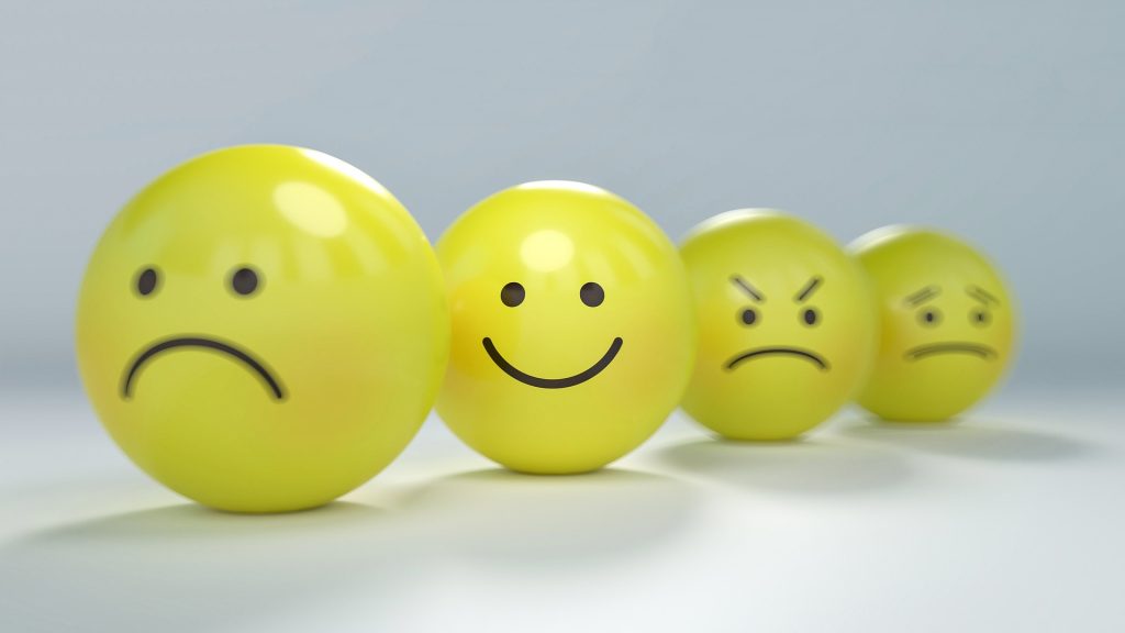 Four yellow balls with faces on. The smiling face is in focus while sad and angry ones are out of focus.